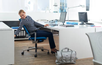 kobieta na niebieskim fotelu biurowym wokół eleganckich białych mebli biurowych
