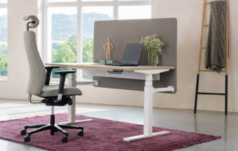 szary wysoki fotel biurowy przy nowoczesnym biurku z regulacją wysokości i brązową ścianką
